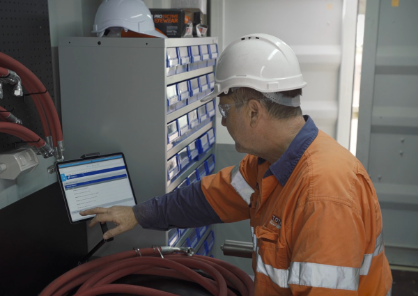 Total Fire Solutions team member in protective clothing demonstrating the reporting system inside the TFS container workshop.